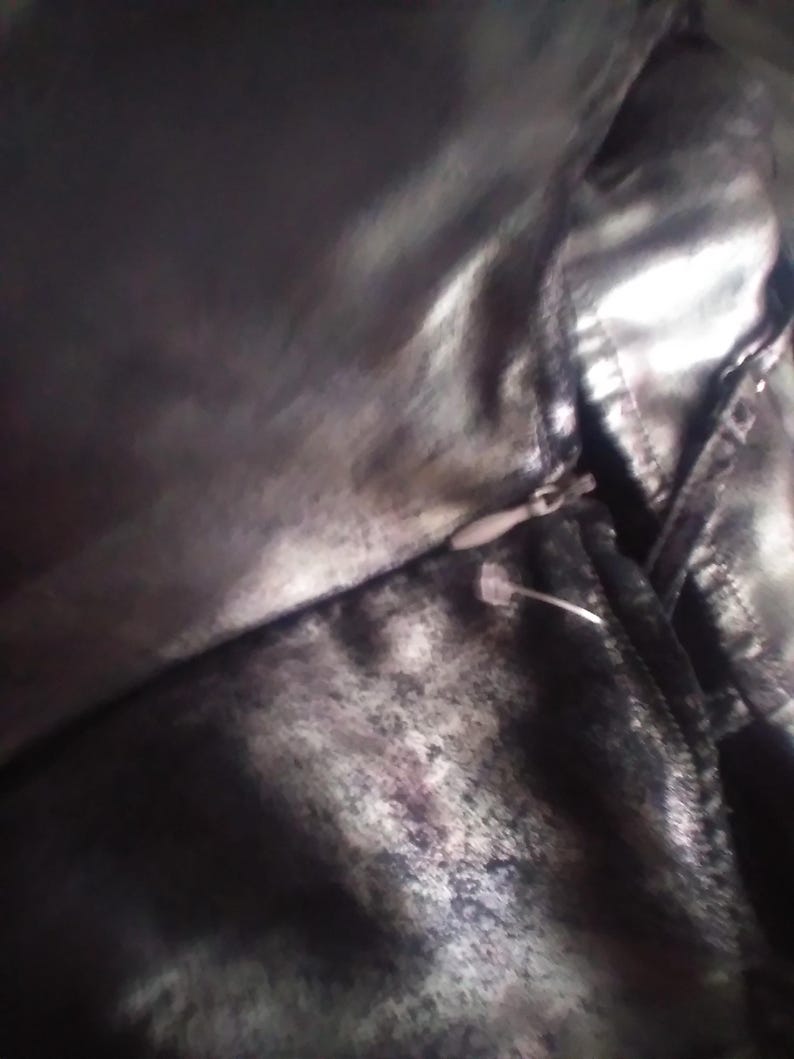 May include: A close-up of a black and silver fabric with a zipper. The fabric has a textured, almost metallic look.
