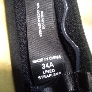 May include: Close-up of a black strapless bra with a label that reads "MADE IN CHINA", "34A", and "LINED STRAPLESS". The label also indicates the fabric composition: 84% nylon and 16% Lycra&reg; spandex.