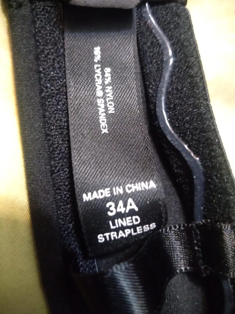 May include: Close-up of a black strapless bra with a label that reads "MADE IN CHINA", "34A", and "LINED STRAPLESS". The label also indicates the fabric composition: 84% nylon and 16% Lycra&reg; spandex.