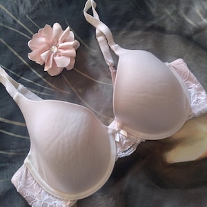 May include: A pale pink bra with delicate lace trim and a small bow detail. The bra has adjustable straps and a hook and eye closure.