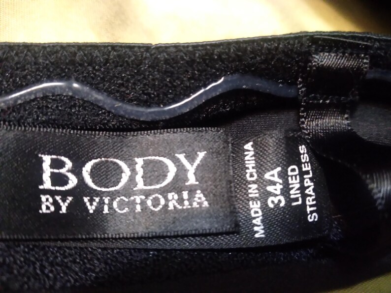 May include: Black strapless bra with the text "BODY BY VICTORIA" on a tag. The tag also indicates a 34A size and "MADE IN CHINA". The bra is lined.