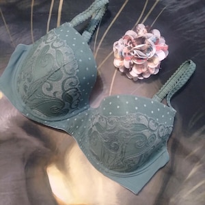 May include: A green bra with white polka dots and lace detailing. The bra has adjustable straps and a hook and eye closure.