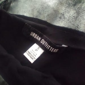 May include: A black clothing tag with white text that reads "Urban Outfitters" and "S P" with the text "Made in Vietnam" and "Fabriqu&eacute; au Vietnam" below.