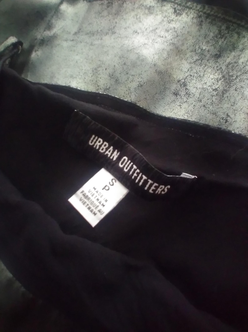May include: A black clothing tag with white text that reads "Urban Outfitters" and "S P" with the text "Made in Vietnam" and "Fabriqu&eacute; au Vietnam" below.