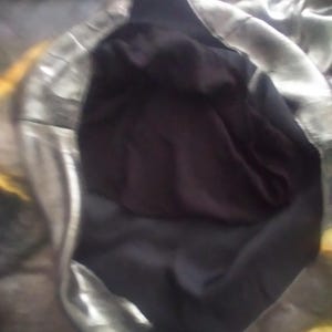 May include: A silver and black fabric garment with a hood. The hood is lined with black fabric.