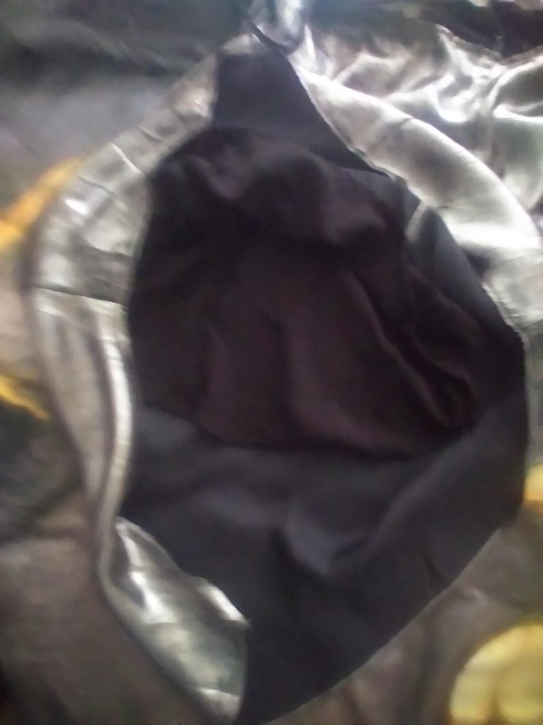 May include: A silver and black fabric garment with a hood. The hood is lined with black fabric.