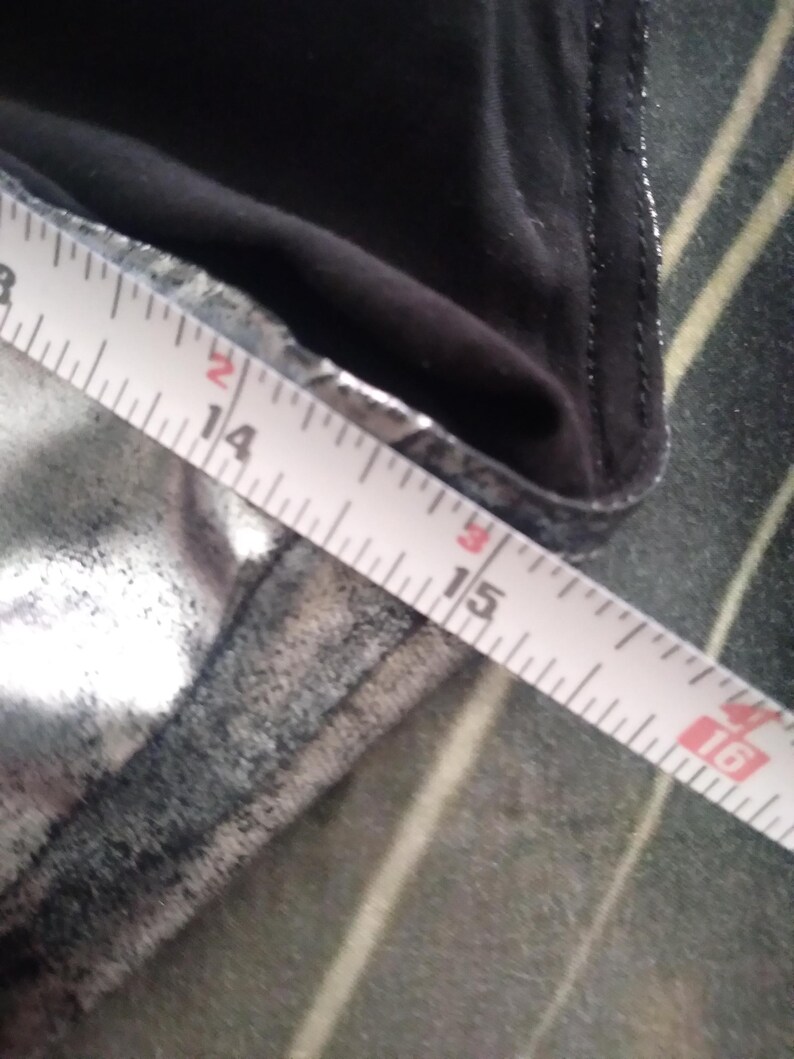 May include: A close-up of a silver fabric with a black seam. A white measuring tape is laid across the fabric, showing measurements from 14 to 16 inches.
