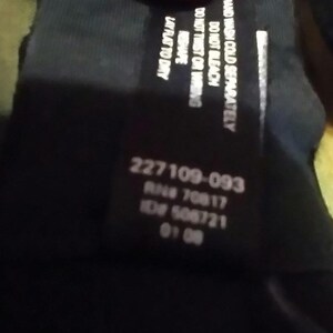 May include: A black clothing tag with white text. The tag includes care instructions: "HAND WASH COLD SEPARATELY, DO NOT BLEACH, DO NOT TWIST OR WRING, RESHAPE, LAY FLAT TO DRY." It also has the numbers "227109-093", "RN# 70817", "ID# 506721", and "01 08".