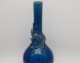 May include: A blue ceramic vase with a bulbous base and a long, slender neck. A detailed dragon design wraps around the vase. The vase is approximately 30 cm tall.