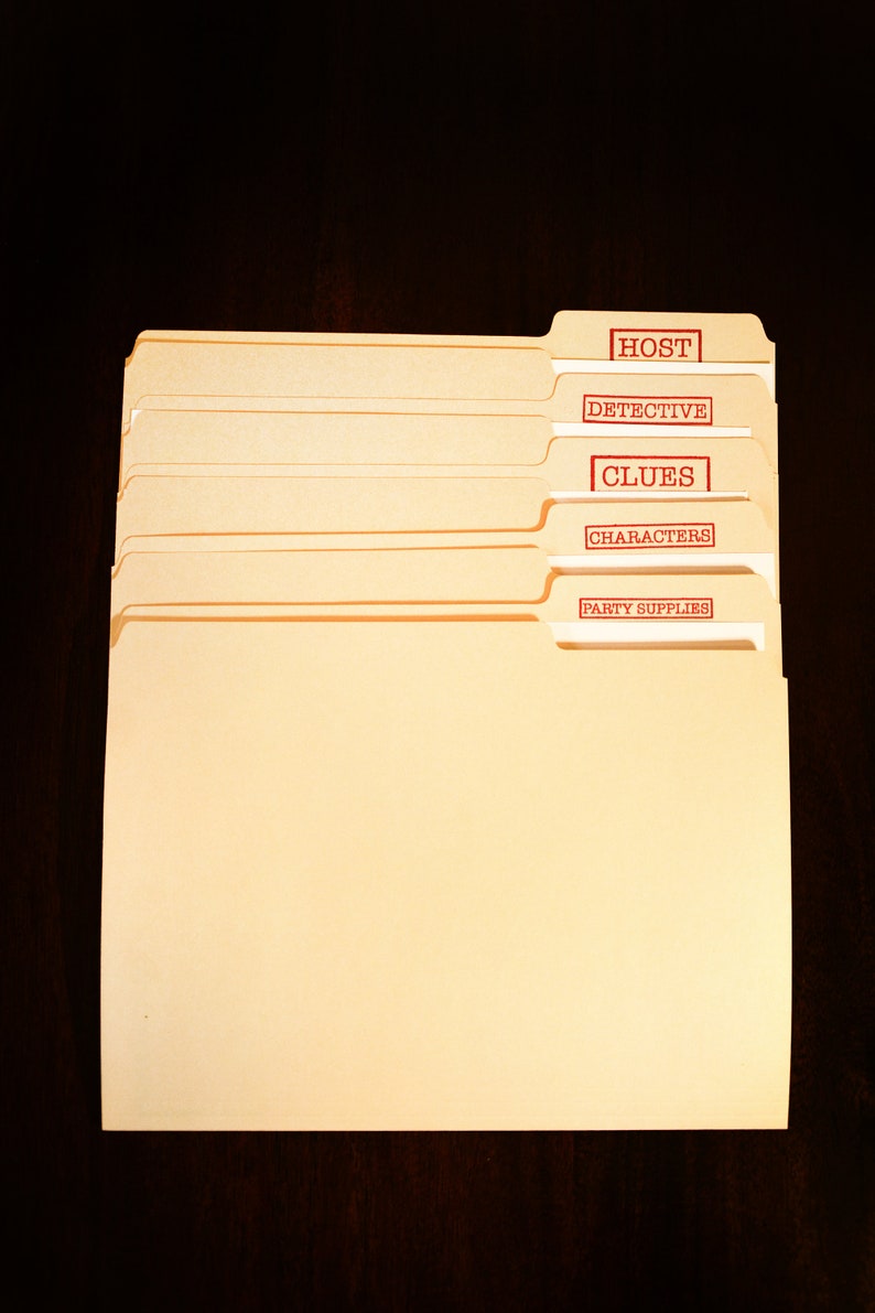 May include: A collection of manila file folders with red text labels. The labels read "HOST", "DETECTIVE", "CLUES", "CHARACTERS", and "PARTY SUPPLIES". The folders are placed on a dark brown surface.