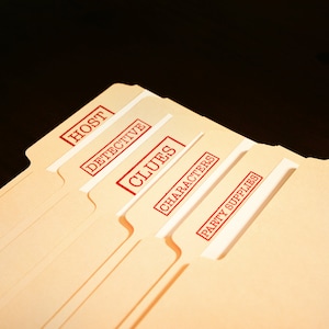 May include: A collection of tan file folders, each labelled with red stamps. The stamps read "HOST", "DETECTIVE", "CLUES", "CHARACTERS", and "PARTY SUPPLIES". The folders are fanned out against a dark backdrop.