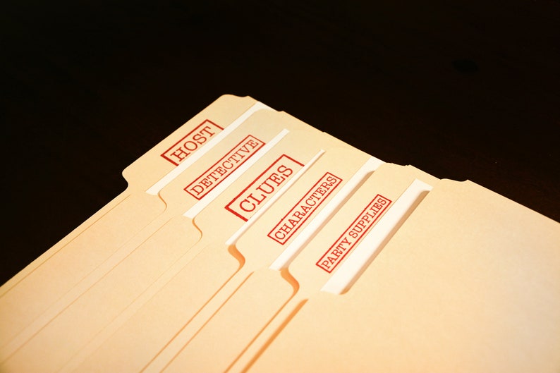 May include: A collection of tan file folders, each labelled with red stamps. The stamps read "HOST", "DETECTIVE", "CLUES", "CHARACTERS", and "PARTY SUPPLIES". The folders are fanned out against a dark backdrop.