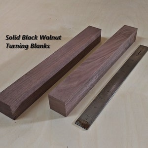 May include: Two solid black walnut turning blanks, each measuring approximately 10 inches long, are shown next to a ruler.  The wood has a rich brown color and a natural grain pattern.  Solid Black Walnut Turning Blanks.