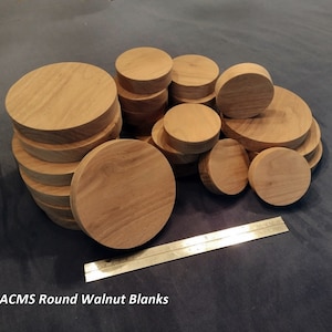 May include: A collection of round, unfinished walnut wood blanks in various sizes. The blanks are stacked and arranged, with a brass ruler for scale. The text "ACMS Round Walnut Blanks" is visible at the bottom.
