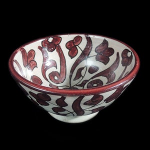 May include: A white ceramic bowl with a red and brown floral design. The bowl has a rounded shape and a slightly flared rim.