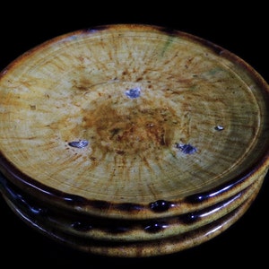 May include: Three stacked ceramic plates with a brown rim and a yellow glaze. The plates have a rustic, handmade look with a mottled, uneven glaze.