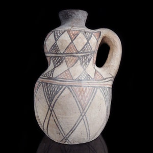 May include: A brown ceramic jug with a geometric pattern in black, white, and red. The jug has a rounded body and a handle.
