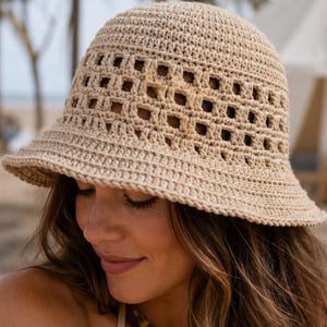 Puede incluir: Un sombrero de cubo de ganchillo beige con ala ancha y cortes cuadrados. El sombrero está hecho de un hilo suave y texturizado. Este accesorio es perfecto para la playa o el uso diario. Protege del sol.