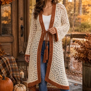 May include: A long, open-front crochet cardigan in cream with rust-colored trim and a matching tie closure featuring tassels. The garment has long sleeves and a loose, open-knit pattern, worn over a white top and blue denim jeans with brown boots.