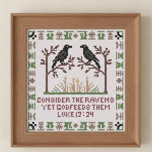 May include: Cross-stitch artwork in a wooden frame. The design features two black ravens perched on branches, with text that reads "Consider the ravens, yet God feeds them, Luke 12:24." The artwork uses green, brown, and black thread.