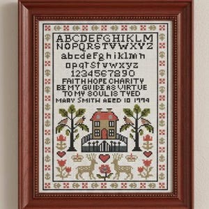 May include: A framed cross-stitch sampler with a dark wood frame. The sampler features an alphabet, numbers, and a verse. Below the text is a house, trees, deer, and floral motifs. The text reads "FAITH HOPE CHARITY BE MY GUIDE AS VIRTUE TO MY SOUL IS TYED MARY SMITH AGED 10 1774".