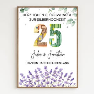 May include: A framed print with the text "HERZLICHEN GLÜCKWUNSCH ZUR SILBERHOCHZEIT" and "25" in large numbers filled with Euro banknotes. Below, it reads "Julia & Jonathan" and "HAND IN HAND EIN LEBEN LANG". Lavender flowers and greenery decorate the edges.