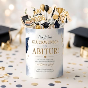 Peut inclure: Une boîte cadeau cylindrique de remise de diplôme avec le texte allemand Herzlichen GLÜCKWUNSCH ZUM ABITUR! et des découpes décoratives de livres, un trophée doré, une toque, des ballons, un globe et une clé sur fond blanc et bleu.