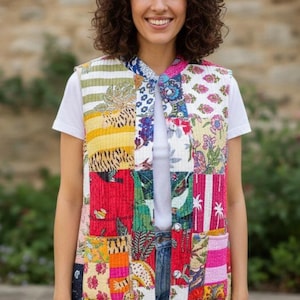 Può includere: Un gilet patchwork con una varietà di motivi colorati, tra cui disegni floreali e geometrici. Il gilet è indossato sopra una maglietta bianca e jeans blu. Il gilet ha un collo e due tasche anteriori.
