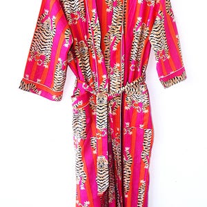 May include: A pink and orange silk robe with a tiger print and striped pattern. The robe has a tie belt and long sleeves.
