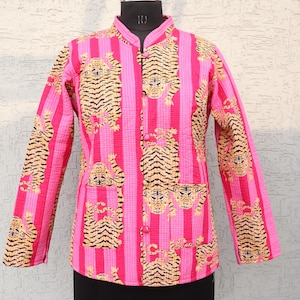 May include: A pink quilted jacket with a vertical striped pattern and tiger illustrations. The jacket has long sleeves, a mandarin collar, and two front pockets. It is buttoned up the front and displayed on a black mannequin.