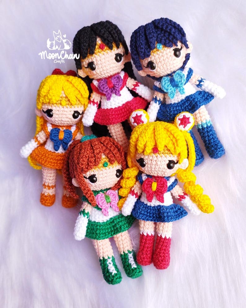 May include: Five crocheted Sailor Moon character dolls. The dolls are all wearing their signature outfits and have bright colors. The dolls are all smiling and have big eyes.