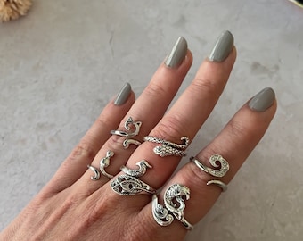 Peut inclure: Une main portant un ensemble de bagues en argent avec différents motifs, dont un serpent, un chat et un oiseau. Les bagues sont portées sur différents doigts.