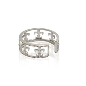 May include: A silver-toned cuff bracelet featuring a fleur-de-lis design. The open-ended bracelet has a rectangular section with the fleur-de-lis pattern and a beaded border. The design is repeated around the bracelet's circumference.