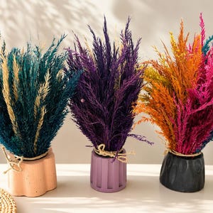 May include: Three decorative floral arrangements in colorful hues. The first features teal and beige, the second purple, and the third orange, yellow, and pink. Each arrangement is in a unique, textured pot, tied with twine, and suitable for home decor.