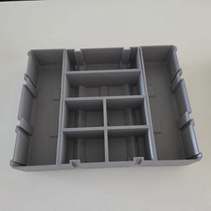 May include: A grey plastic organiser with multiple compartments and dividers. The organiser has a rectangular shape with various sized sections, designed for storage and organisation. The compartments are arranged in rows and columns, providing a structured storage solution.