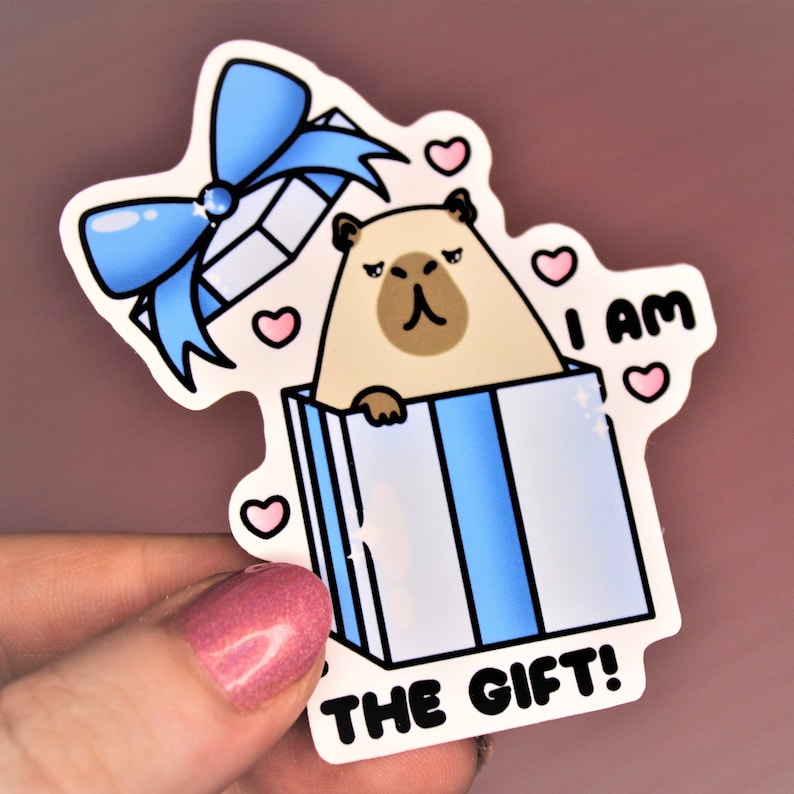 Op de afbeelding: Een sticker met een cartoonillustratie van een hond in een blauwe en witte cadeaudoos. De hond kijkt uit de doos en de tekst "Ik ben het cadeau!" staat onder de doos.