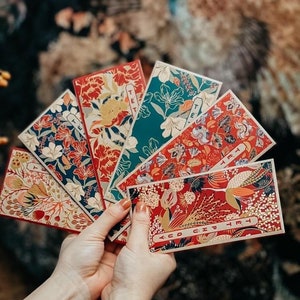May include: Five red and gold patterned envelopes with the word "Tết" written on them. The envelopes are held in a hand.