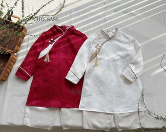 Può includere: Due camicie tradizionali cinesi per bambini, una rossa e una bianca, con pantaloni bianchi abbinati. Le camicie hanno un colletto alla coreana e un fiocco decorativo.