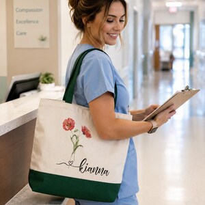 A smiling woman in blue scrubs stands in a hallway, holding a clipboard and wearing a tote bag with a floral design.
