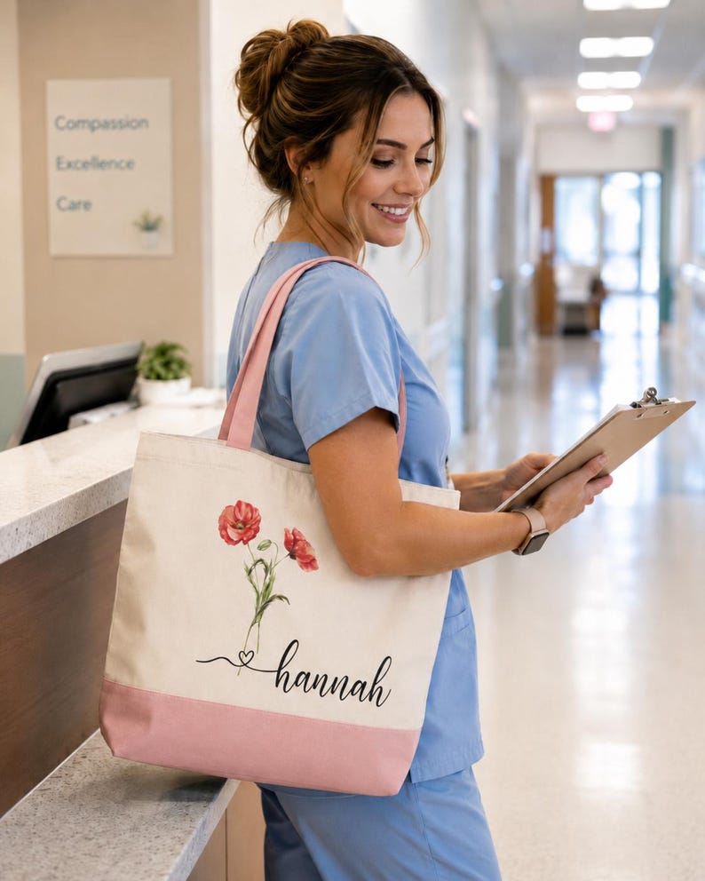 A smiling woman in blue scrubs is standing in a hallway, holding a clipboard and a bag with a floral design.