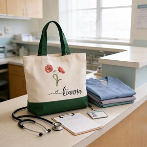 A green and white tote bag with a floral design and the name "Kianna" printed on it, along with a stethoscope, clipboard, and medical scrubs, all placed on a counter in a medical setting.