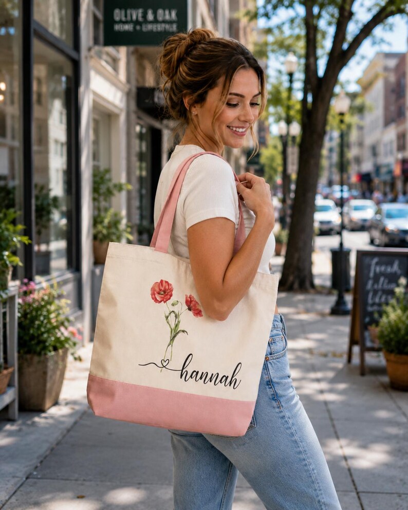 A woman is standing on a sidewalk, smiling and carrying a pink and white tote bag with a floral design.