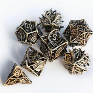 May include: A set of antique bronze-colored metal dice with leaf and number details. The dice include various shapes, such as a d20, d12, d10, d8, and d4, suitable for tabletop role-playing games. The dice are arranged on a white surface.