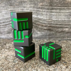 May include: Four gray and green geometric cubes are stacked and arranged on a textured surface. The cubes have a dark gray exterior with bright green linear accents. One cube is separate from the stack. The cubes are a modern design.