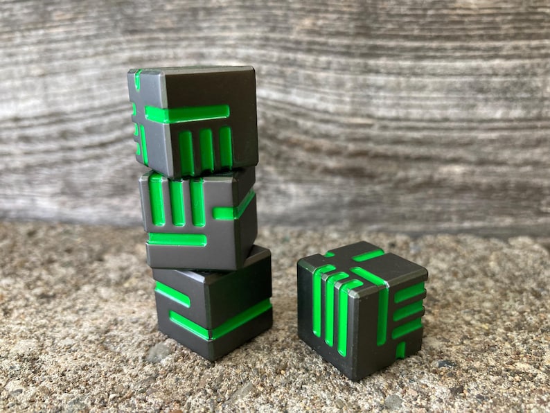 May include: Four gray and green geometric cubes are stacked and arranged on a textured surface. The cubes have a dark gray exterior with bright green linear accents. One cube is separate from the stack. The cubes are a modern design.