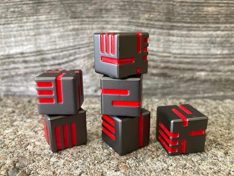 May include: Six dark gray, cube-shaped objects with red accents are stacked and arranged on a textured surface. The cubes have a geometric design with red lines and shapes. The overall aesthetic is modern and minimalist.