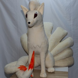 May include: A large, plush, white fox with a fluffy tail. The fox has red eyes and a long, orange tail.