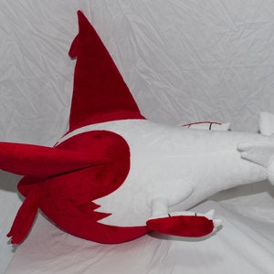 Puede incluir: Un juguete de peluche de un dragón rojo y blanco con una cola larga y alas. El dragón tiene un ojo amarillo y una barriga blanca.