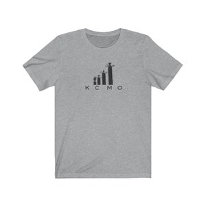 Op de afbeelding: Een grijs t-shirt met een zwart silhouet van de skyline van Kansas City en de letters "KCMO" eronder.