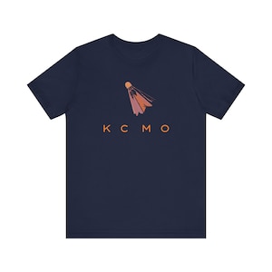Könnte beinhalten: Ein marineblaues T-Shirt mit einer orangefarbenen Badminton-Federballgrafik und dem Text "KCMO" in Orange.